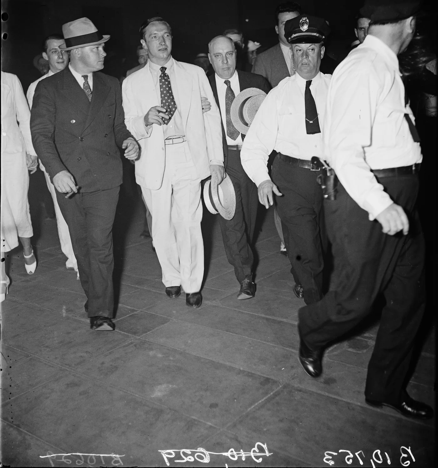 Marion Zioncheck in a light suit walking under escort beside a uniformed Capitol police officer